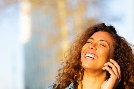 Close up portrait of cheerful young latin female talking on cellphone outdoors in cityの写真素材