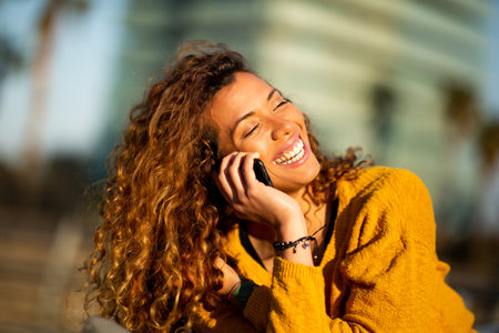 Close up portrait of laughing young latin female talking on cellphone outdoors in cityの写真素材