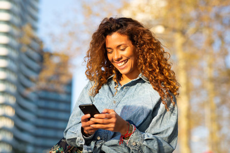 Portrait of beautiful young latin woman with phone walking in cityの写真素材