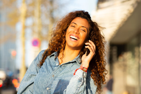 Close up portrait of smiling young woman talking on mobile phone walking outdoors in the cityの写真素材