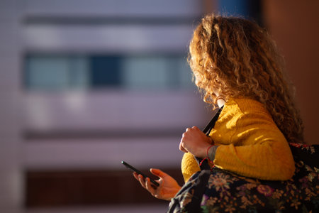 Side portrait of young woman walking with bag and mobile phone outside in the cityの写真素材