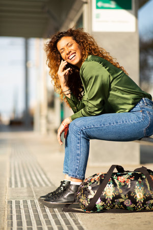 Portrait of attractive young female traveller talking on phone while waiting for tram at stationの写真素材