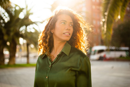 Portrait of beautiful young woman looking away standing outside in the city on a sunny dayの写真素材