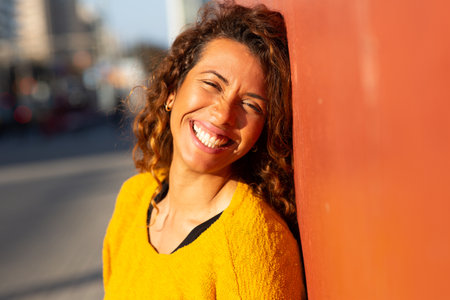 Close up portrait of beautiful young latin leaning against wall looking at camera and smilingの写真素材