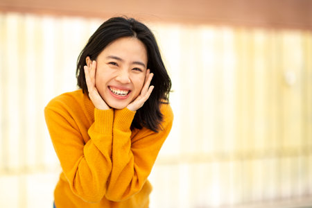 Portrait young asian woman smiling with hands on faceの写真素材