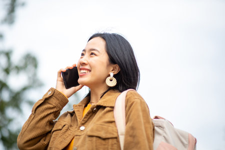Side portrait smiling young asian woman with bag talking on phoneの写真素材