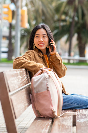 Portrait young asian woman talking with phone while sitting on park benchの写真素材