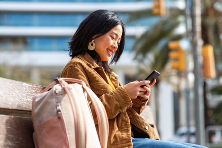Portrait young asian woman sitting on bench in city with mobile phone in handの写真素材