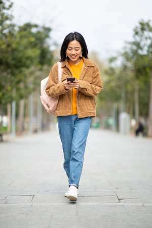 Full body portrait young woman walking with mobile phone and bagの写真素材