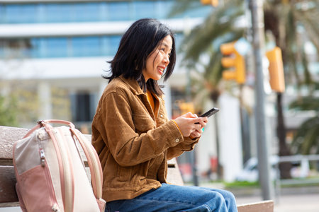 Portrait young asian woman using mobile phone while sitting on benchの写真素材