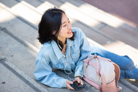 Portrait young woman sitting with mobile phone and listening to music with earphonesの写真素材