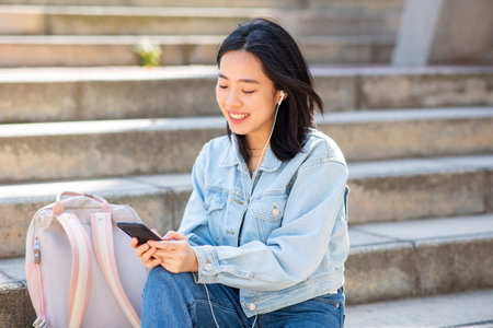 Portrait smiling young woman sitting with phone outsideの写真素材