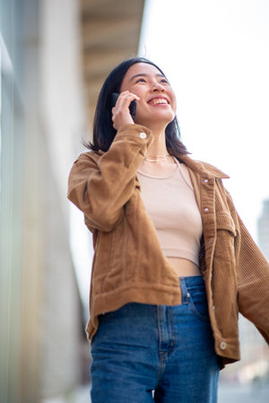 Portrait smiling young woman walking in city with mobile phoneの写真素材