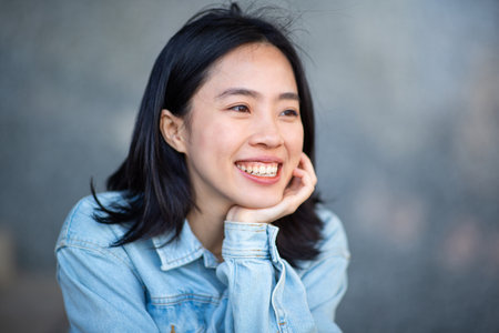 Portrait smiling young asian woman with hand on chin and looking awayの写真素材