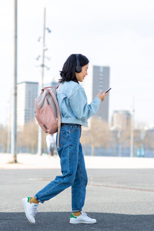 Full body side portrait young woman walking with bag and mobile phoneの写真素材