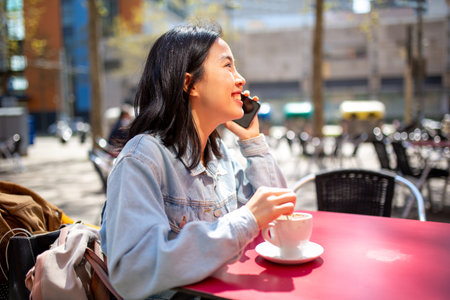 Portrait smiling young woman sitting at cafe talking with mobile phoneの写真素材