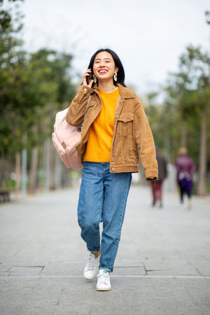 Full body portrait smiling young woman walking with mobile phone and bagの写真素材