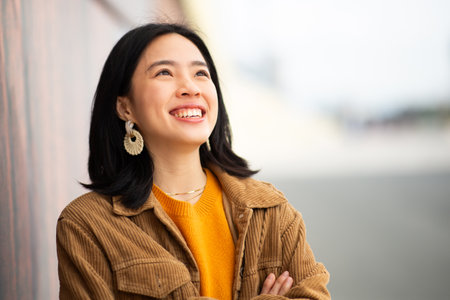 Portrait young asian woman smiling with arms crossed and looking upの写真素材
