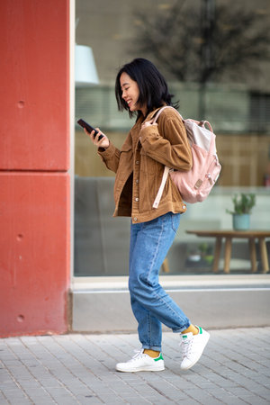 Full body portrait young woman walking bag and mobile phoneの写真素材