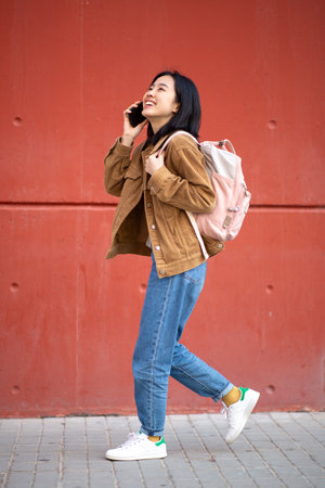 Full body portrait happy young woman walking bag and talking with mobile phoneの写真素材