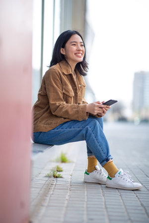 Portrait smiling young woman sitting with mobile phone in cityの写真素材