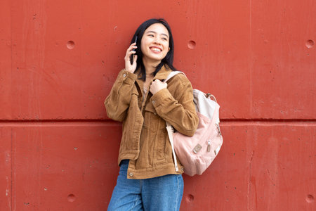 Portrait smiling young woman talking with mobile phone by wallの写真素材