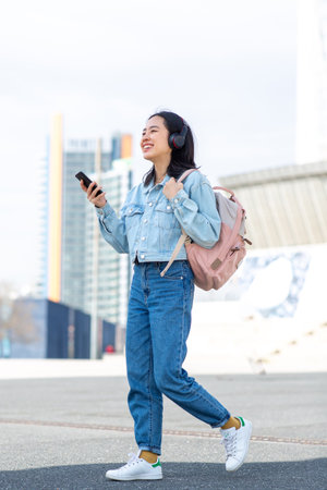 Full body portrait young woman walking with bag and mobile phoneの写真素材