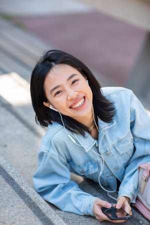 Portrait smiling young woman sitting with mobile phone and listening with earphonesの写真素材
