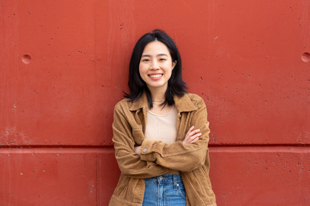 Portrait young asian woman smiling by wall with arms crossedの写真素材