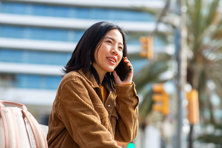 Portrait young asian woman talking with mobile phone while sitting on benchの写真素材