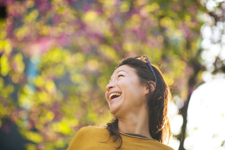 Close-up portrait of cheerful young asian woman looking away and laughing standing outsideの写真素材
