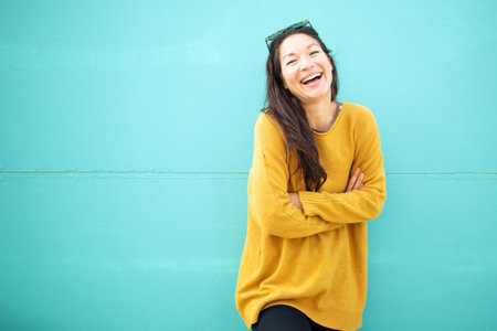 Portrait of young woman with her arms crossed looking at camera and smiling against green wallの写真素材