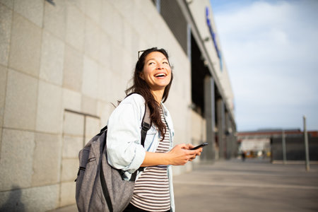 Portrait of cheerful young asian woman with mobile phone standing in the city