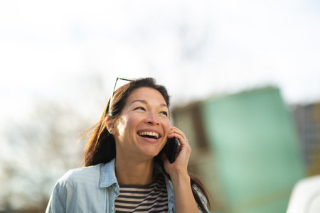 Close-up portrait of attractive young asian woman making a phone call while walking outside in the cityの写真素材