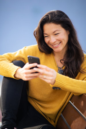 Portrait of pretty young asian woman sitting on bench and using mobile phone