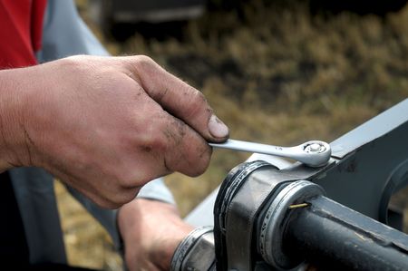 man's hand reapiring harvester whith wrench on field