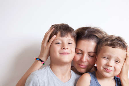 Portrait of happy mother with cute kids boy sitting on a light background. Happy family concept.