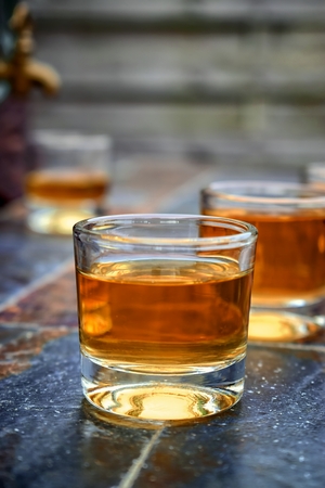 Alcohol, taste and drink concept-glasses with whiskey, old glass barrel on a stone table and wooden background.の写真素材