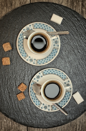 Drinks, drinking, energy and caffeine concept-two cups of coffee on a dark slate stand and wooden background.の写真素材