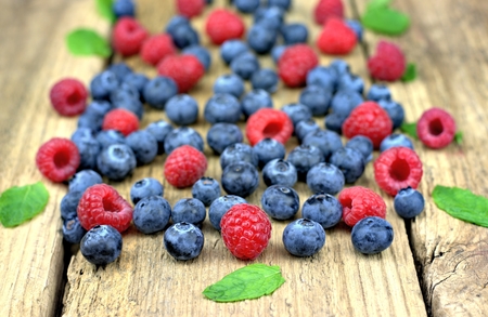 Healthy food, agriculture, harvest and fruit concept: close up view of fresh ripe raspberries and blueberries on an old wooden table.の写真素材