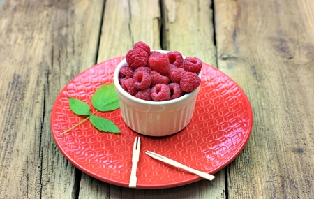 Healthy food, agriculture, harvest and fruit concept: close up view of a plate of red raspberries.