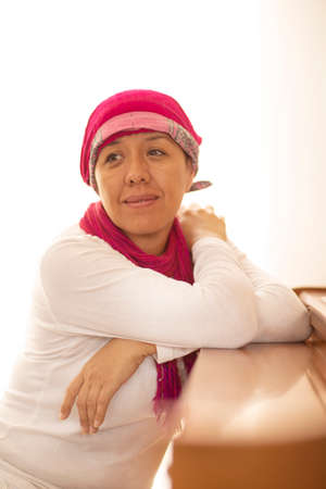 Hispanic lady dressed in white with a pink scarf on her head, thoughtful and happyの写真素材