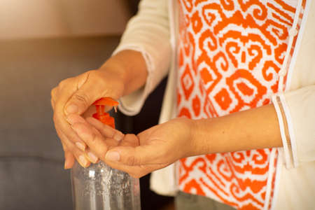 Woman with colored clothes using antibacterial gel with alcohol in home, hand cleaning, protection against corneal diseaseの写真素材
