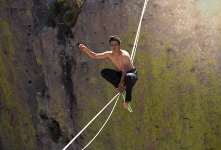 young latino man, doing tightrope walking in mountains, in nature. extreme sports.の写真素材