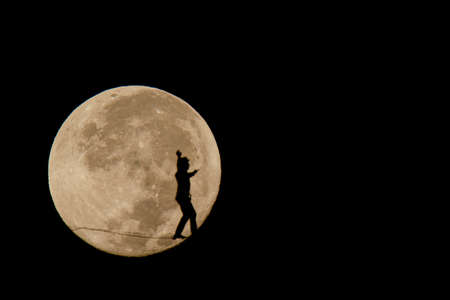 silhouette of a man walking a tightrope in landscape and in the background the full moonの写真素材
