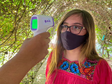 person takes temperature of latina girl in mexican dress, due to the pandemicの写真素材