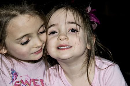 Two little girls playing hugging each other cheek to cheek.