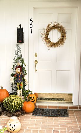 A Fall door adorned with a wreath and surrounded by pumpkins, pinecones and jack-o-laterns.の写真素材