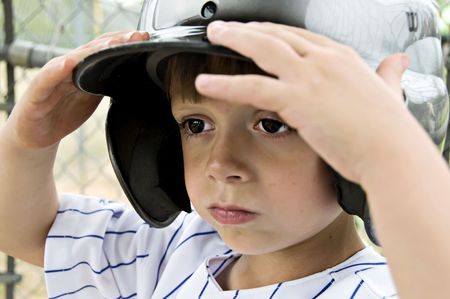 Little boy holding his batting helmet on his head.の写真素材
