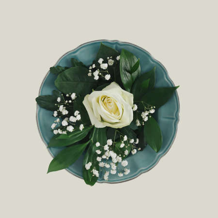 Summer or spring floral weddding layout made with natural white rose and flowers with fresh green leaves on plate, on sandy  pastel background. Minimal flat composition.の写真素材